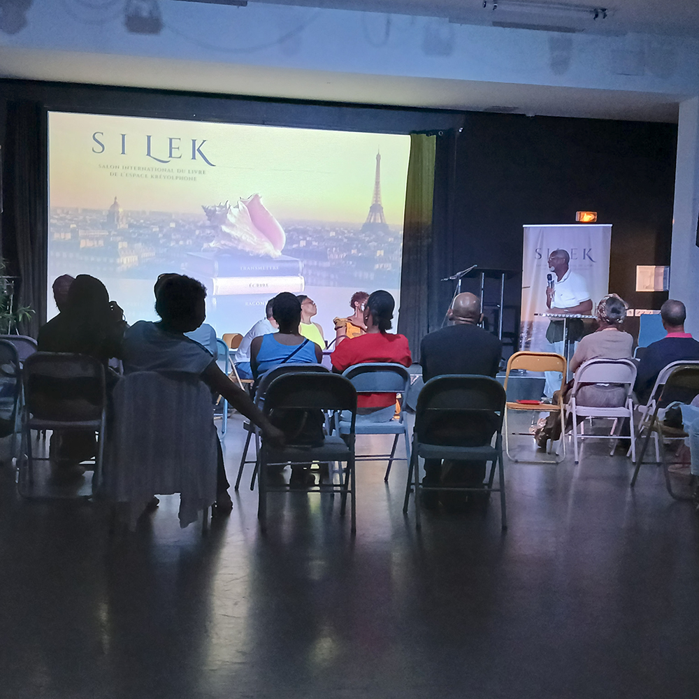 Table ronde du SILEK avec Max Belaise, enseignant-chercheur chargé de mission créole à l’Université des Antilles. Devant l'affiche officielle − 22-24 mai 2026